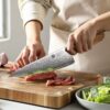 a person cutting meat on a cutting board by using XINZUO B37 Lan Chef's Knife 8.5"
